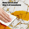 A hand wipes off oil from a yellow substance on a white marble surface using a white wipe.