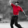 A man in a red shirt and black pants is posing with a clenched fist, looking upward against a blurred background.