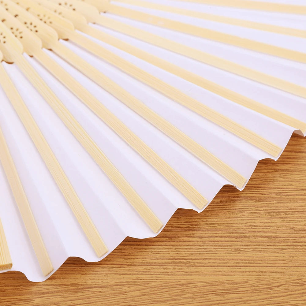 A fan made of light-colored bamboo slats, folded and displayed on a wooden surface.