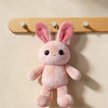 A pink fluffy rabbit hanging from a wooden wall hook rack.