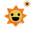 An orange sun-shaped plush toy with a yellow face and black mouth, featuring a small loop for hanging.
