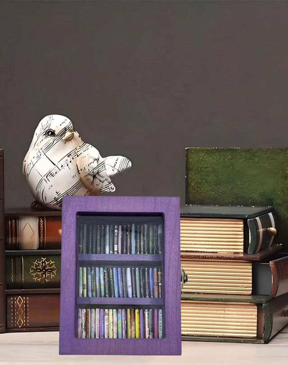 A purple wooden display box holding several books and a white bird figurine.