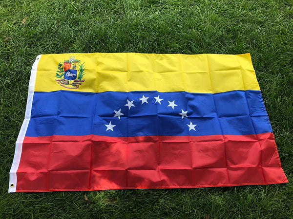 A large Venezuelan national flag banner featuring yellow, blue, and red stripes with stars and a coat of arms, displayed on g