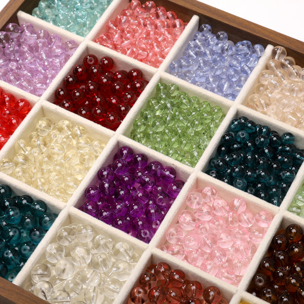 A collection of round glass spacer beads in various colors and shades arranged in small compartments.
