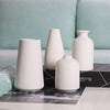 A collection of white ceramic vases and a magazine are displayed on a light surface against a pale blue background.