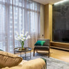A living room interior featuring a sofa and armchair near a large window with sheer curtains.