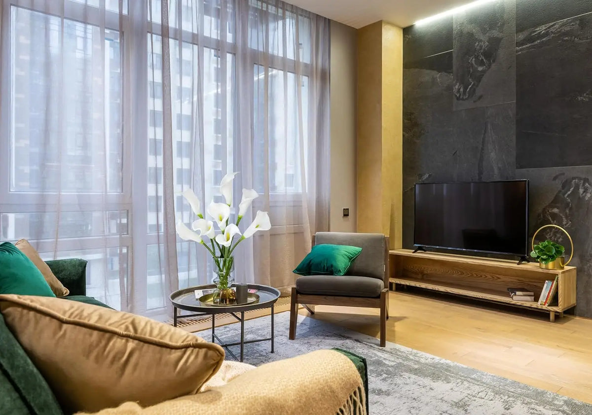 A living room interior featuring a sofa and armchair near a large window with sheer curtains.