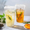Two clear plastic cups filled with iced beverages, one lemon-infused and one orange-infused, resting on a light surface.