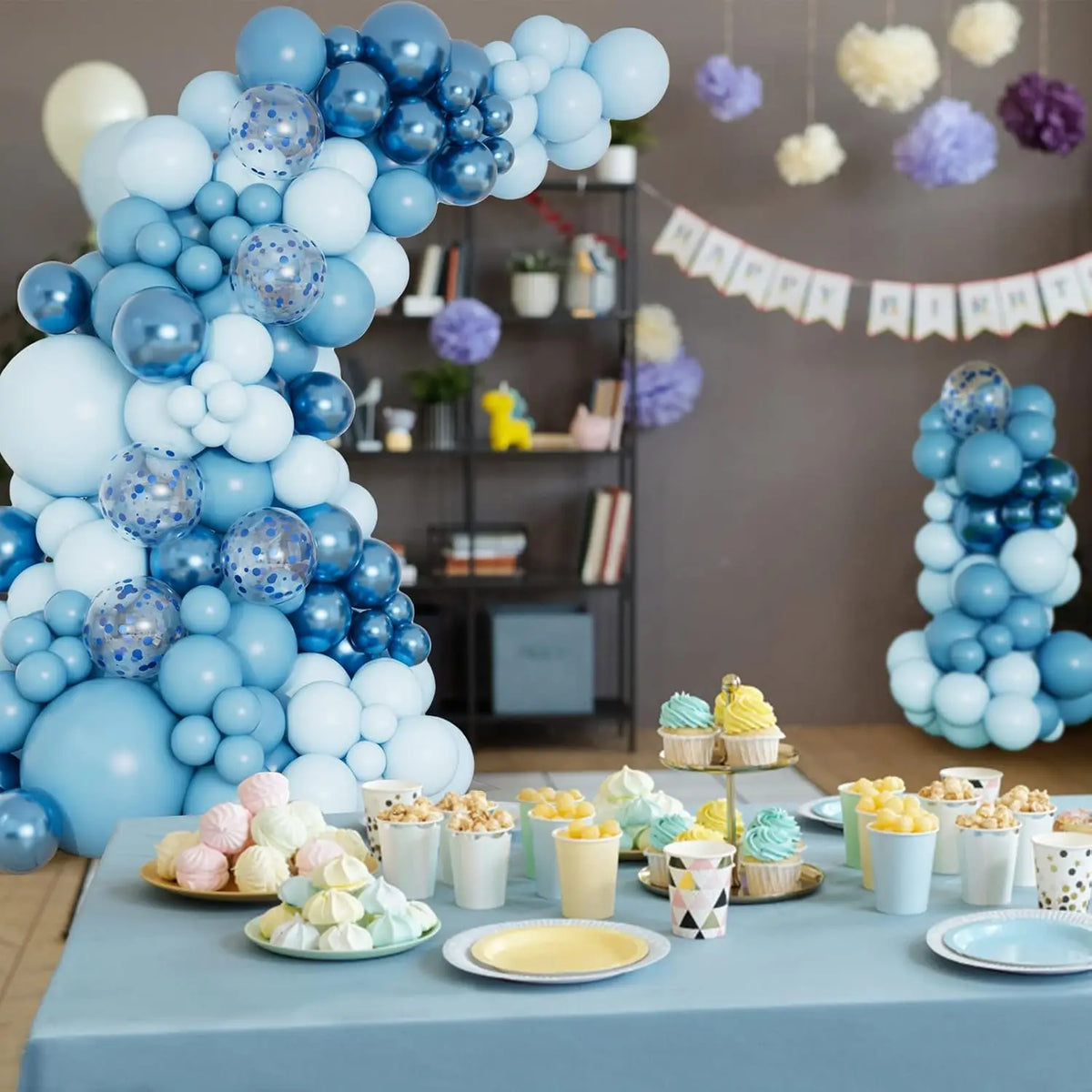 Una gran decoración de columna de globos azules y blancos con varios tonos de globos azules sobre una mesa.