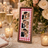 A wooden photo strip frame displaying three small photos of a couple kissing, set in a rustic floral arrangement.