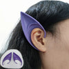 A close-up of a person's ear with realistic purple latex elf ears attached, shown against dark hair.