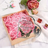 A heart-shaped acrylic decoration featuring a couple silhouette and text, presented in a wooden box with pink shredded paper.