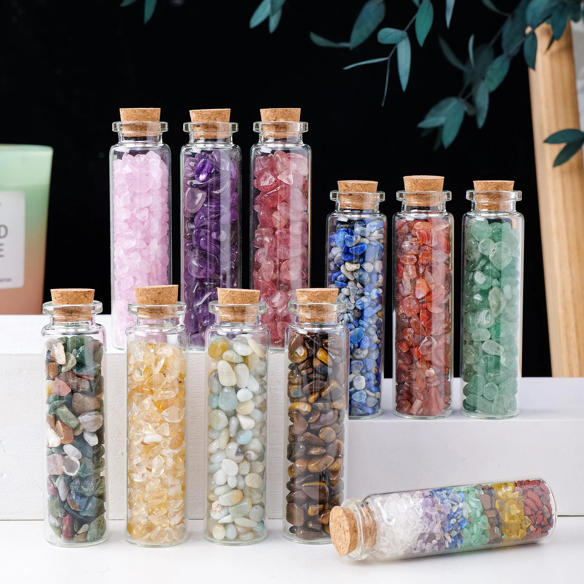 A collection of natural crystal healing bottles in various colors and textures displayed on a white surface.