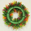 A circular wreath made of artificial flowers in shades of green, orange, and yellow for home decor.