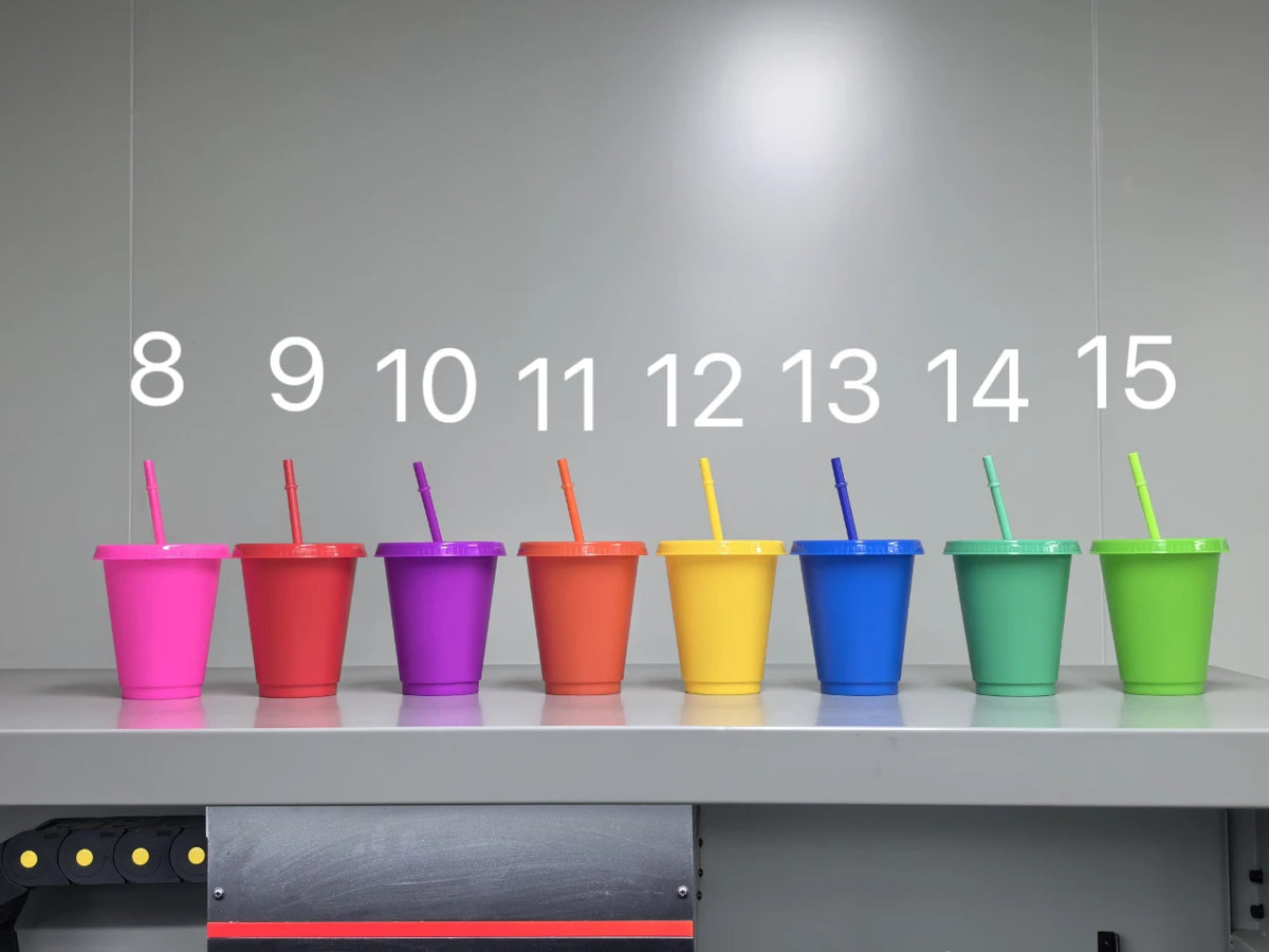 A row of fifteen brightly colored plastic cold cups with lids and straws displayed in a row.