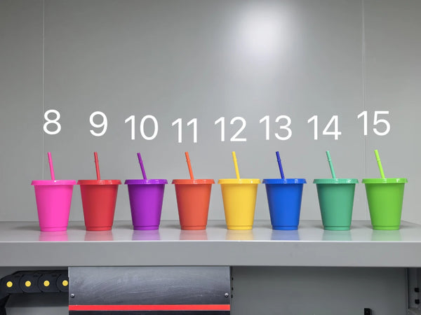 A row of fifteen brightly colored plastic cold cups with lids and straws displayed in a row.