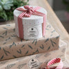 A gift box wrapped in kraft paper with a red and white striped ribbon, sitting on a larger piece of patterned paper.