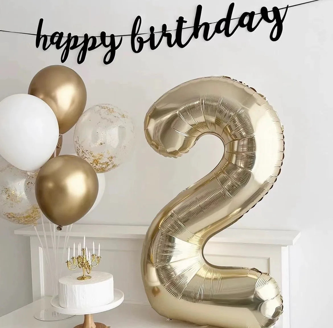 A large champagne gold foil number balloon shaped like the number 2 displayed on a white mantelpiece.