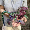 A hand holds a detailed, articulated 3D printed lizard figurine with iridescent green and purple scales.