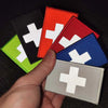 A hand holds several colored IR reflective medical cross tactical morale patches.