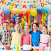 A group of five smiling children posing in front of a colorful balloon arch decoration for a birthday party.