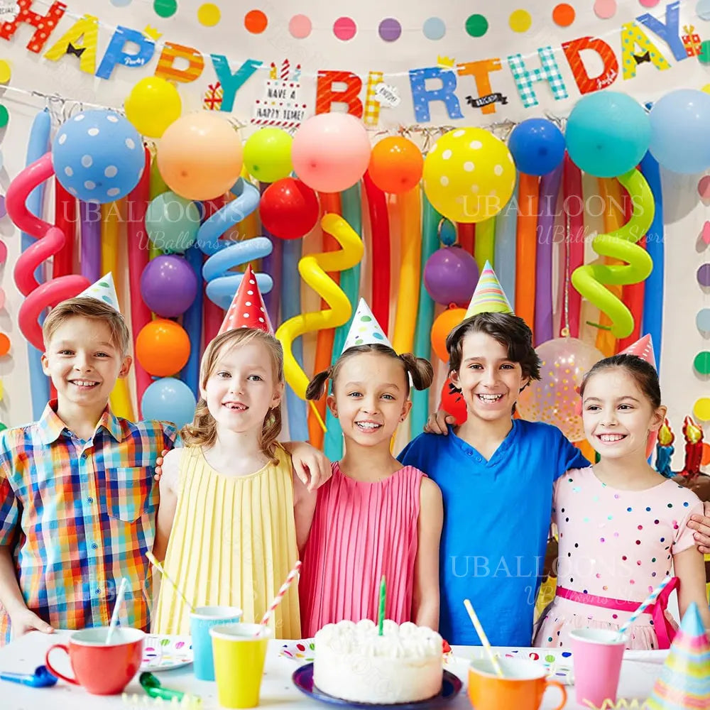 A group of five smiling children posing in front of a colorful balloon arch decoration for a birthday party.