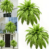 Two large artificial Boston ferns displayed against a white exterior wall.