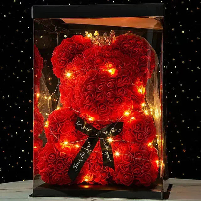 A bright red artificial rose teddy bear illuminated with warm lights inside a clear display box.