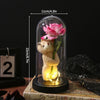 A small, fluffy bear holding a pink rose inside a glass dome with an illuminated base.