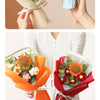 A hand holds a bouquet of handmade sunflower daisy crochet flowers in orange and red paper wrapping.