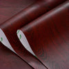 Roll of dark reddish-brown wood grain self-adhesive PVC wallpaper film being peeled from its backing.
