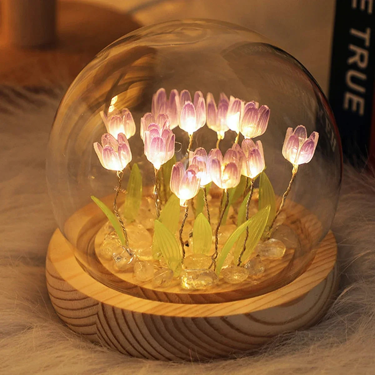 A clear glass globe containing a display of pink LED tulips on a wooden base.