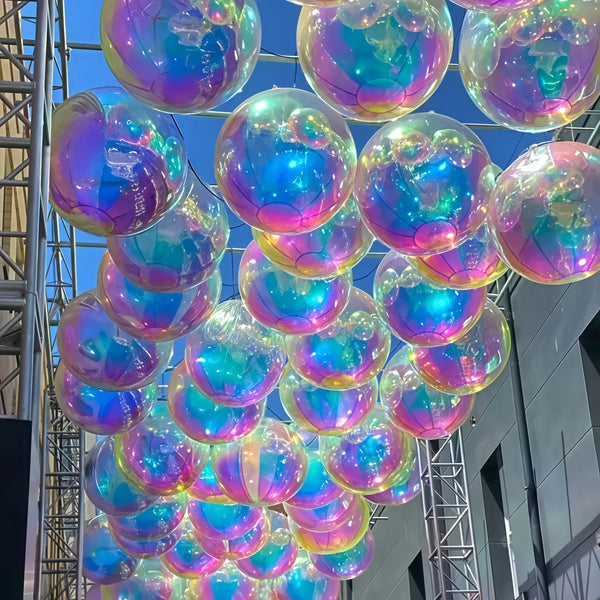 A close-up of numerous iridescent foil balloons in various shades of blue, purple, and green hanging from a metal structure.