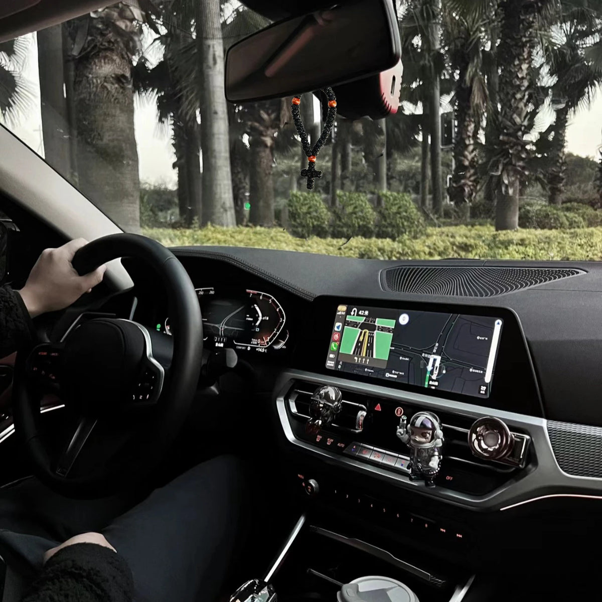 Interior view of a car showing a handmade 33-knot Orthodox prayer rope with a cross charm hanging from the rearview mirror.
