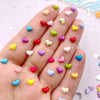 A hand displays a variety of small, flatback heart-shaped rhinestones in various colors for nail art and crafts.