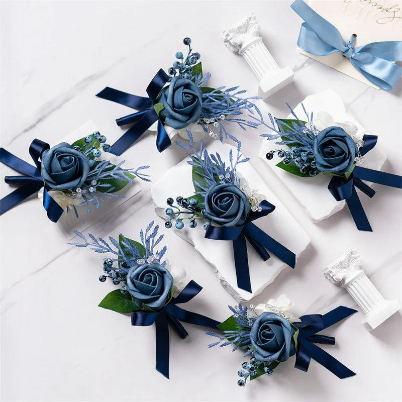 A set of six dusty blue silk rose boutonnieres with navy ribbon and white accents displayed on a white marble surface.