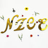 Gold 3D acrylic letter wall stickers spelling NZZE surrounded by small yellow flower and greenery