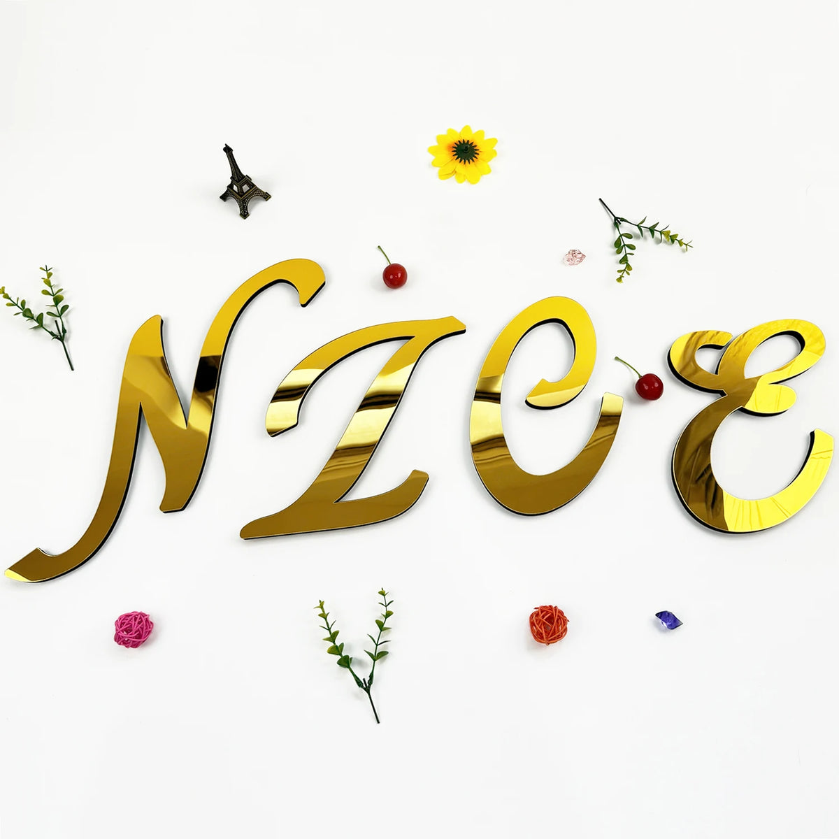 Gold 3D acrylic letter wall stickers spelling NZZE surrounded by small yellow flower and greenery