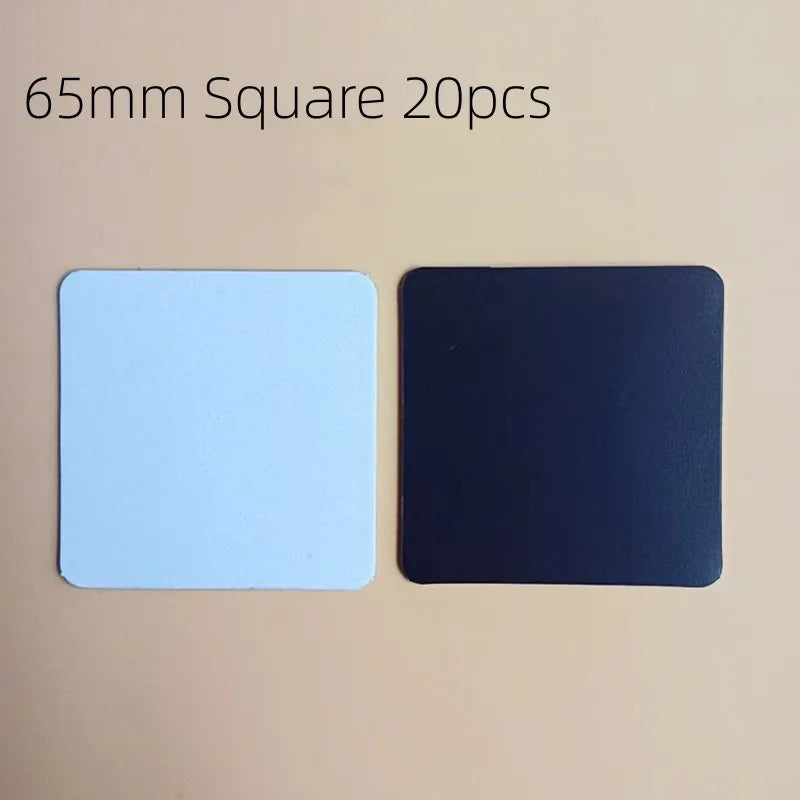 Two 65mm square sublimation fridge magnets, one light blue and one black, displayed on a beige background.