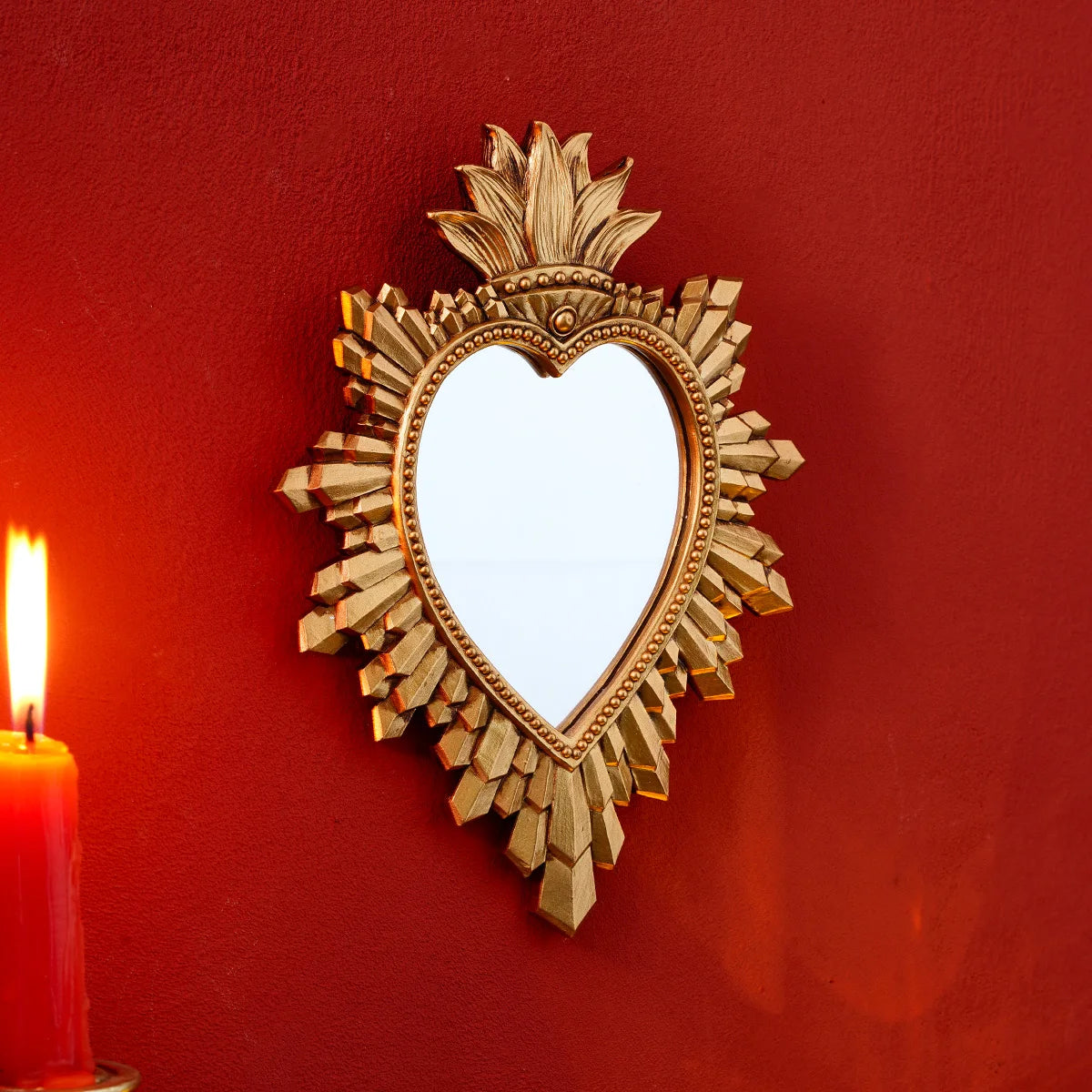 A golden flame sacred heart wall pendant with a resin finish mounted on a red wall.