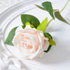 A soft pink velvet artificial rose with green leaves and a bendable stem placed on a white plate.