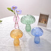 Collection d'objets de décoration en verre de champignons dans des tons de violet, rose, vert et bleu, avec une tige de fleur