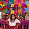 A young woman wearing a white top and red skirt stands in front of colorful papel picado banners.