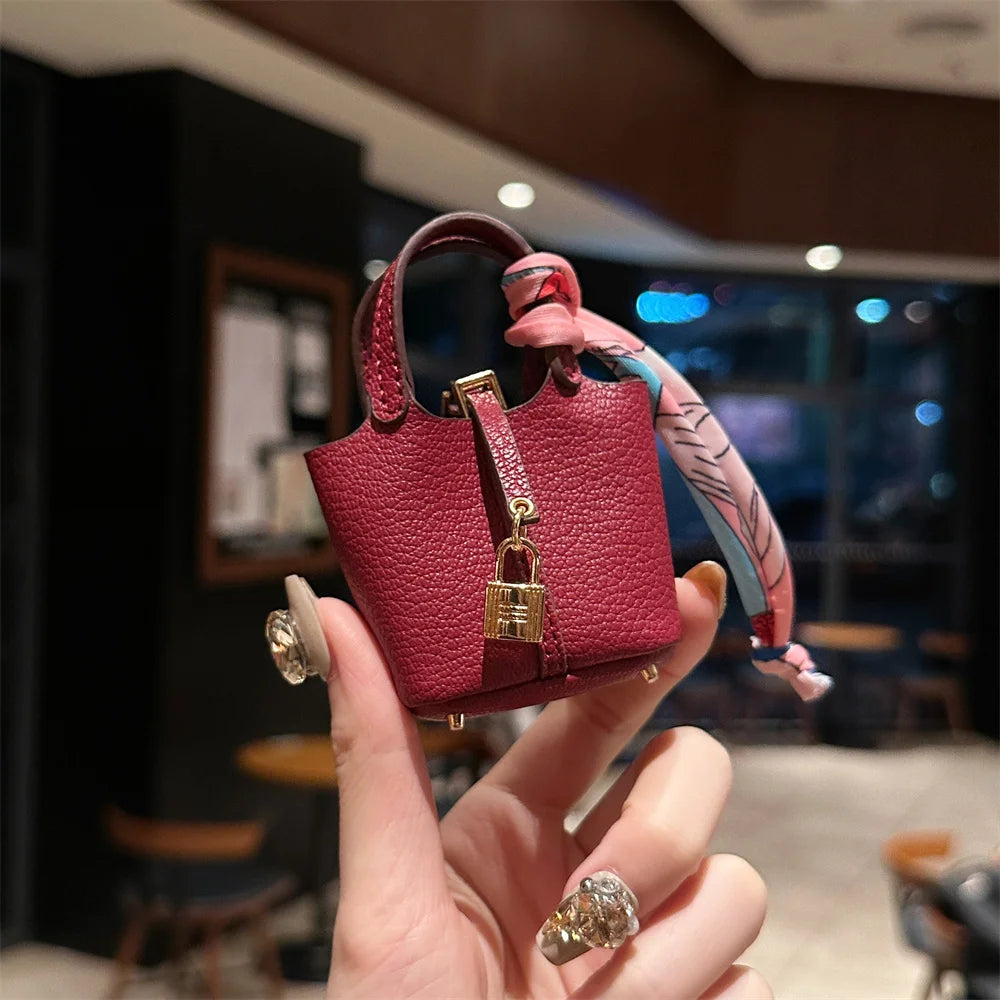 A hand holds a small, deep red leather handbag with a pink patterned wrist strap.