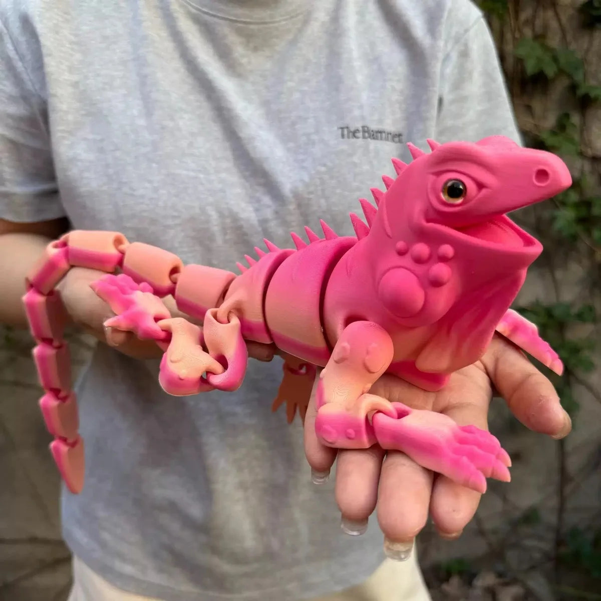 A hand holds a pink, articulated 3D printed lizard figurine for home decor.
