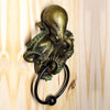 A bronze octopus skull door knocker featuring a cast iron ring mounted on a light wooden surface.
