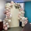 A balloon arch decoration featuring pink, sand, and white balloons for a celebration.