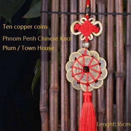 Antique copper five emperor coin pendant with a red Chinese knot hanging from a bamboo rod.