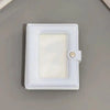 A white mini photo card binder with a clear plastic cover and a silver clasp, resting on a gray surface.