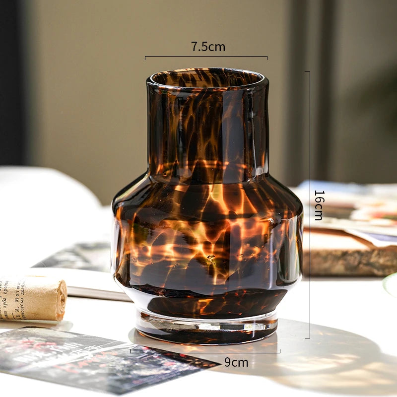 A dark amber glass vase with a leopard print pattern sits on a white surface.